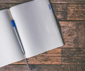 A book sat open on a wooden table with a pen lying in the page crease