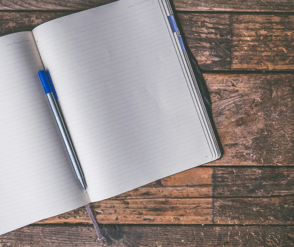 A book sat open on a wooden table with a pen lying in the page crease