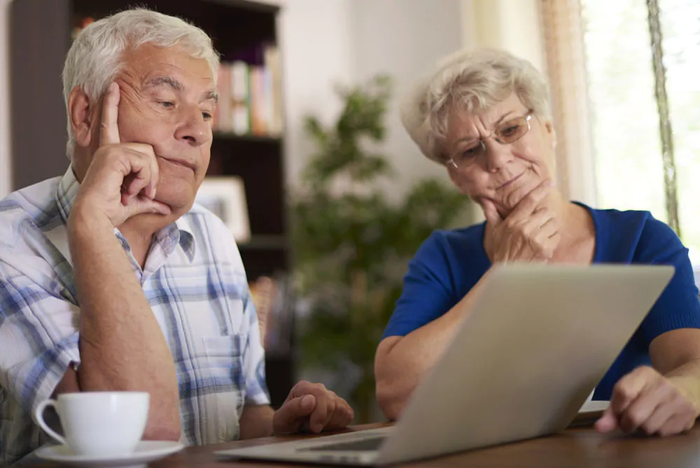 An elderly couple looking inquisative looking at a laptop