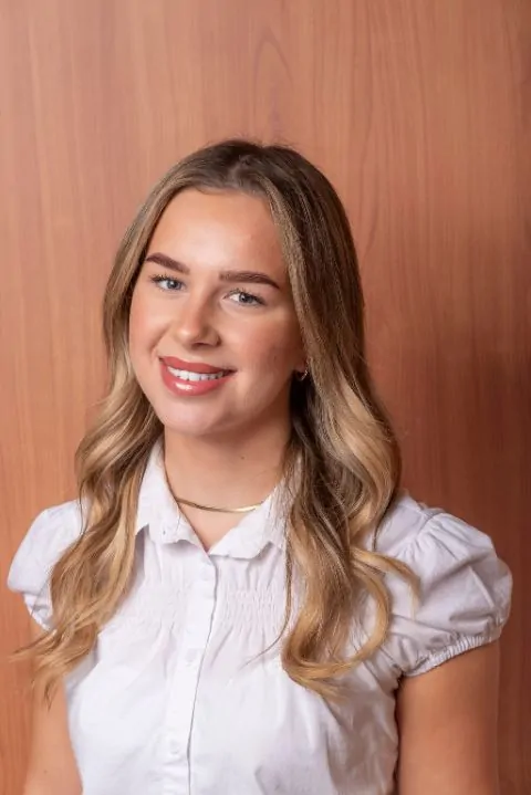 A blonde girl smiling and wearing a white blouse
